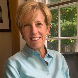 headshot of blog author Christie Peck, sitting near a window with a bright blue shirt on, lightly colored skin, and a short haircut with sandy brown hair