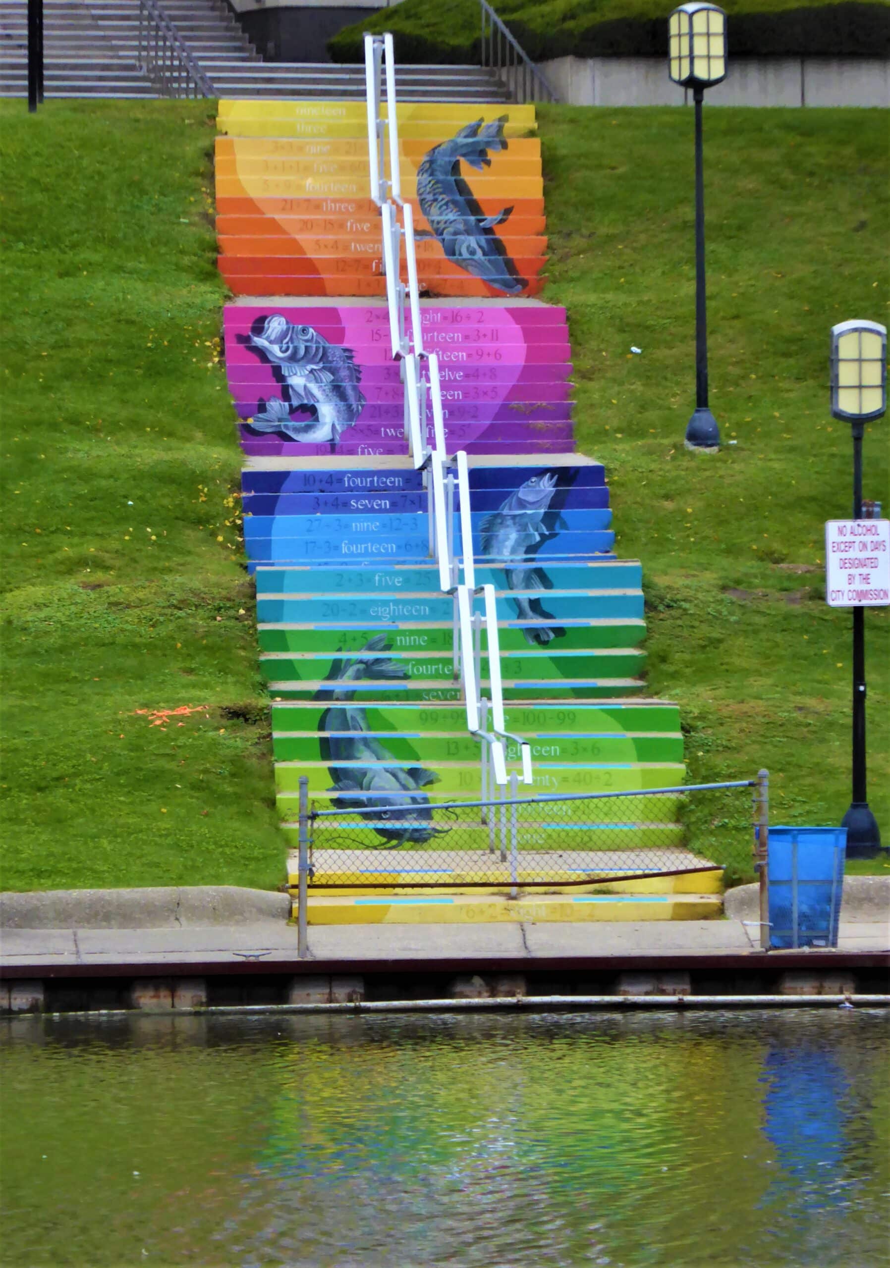 A photo of a mural on stairs that is a rainbow with a few fish jumping painted on top