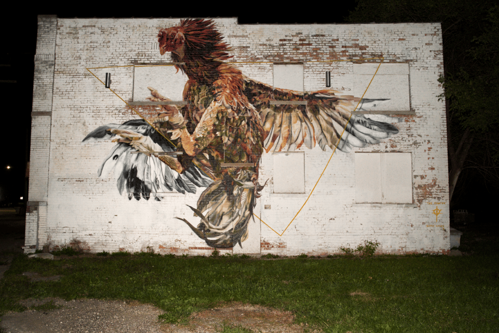 Photo of a mural of a rooster with its wings extended and its talons in the air launching towards the viewer.