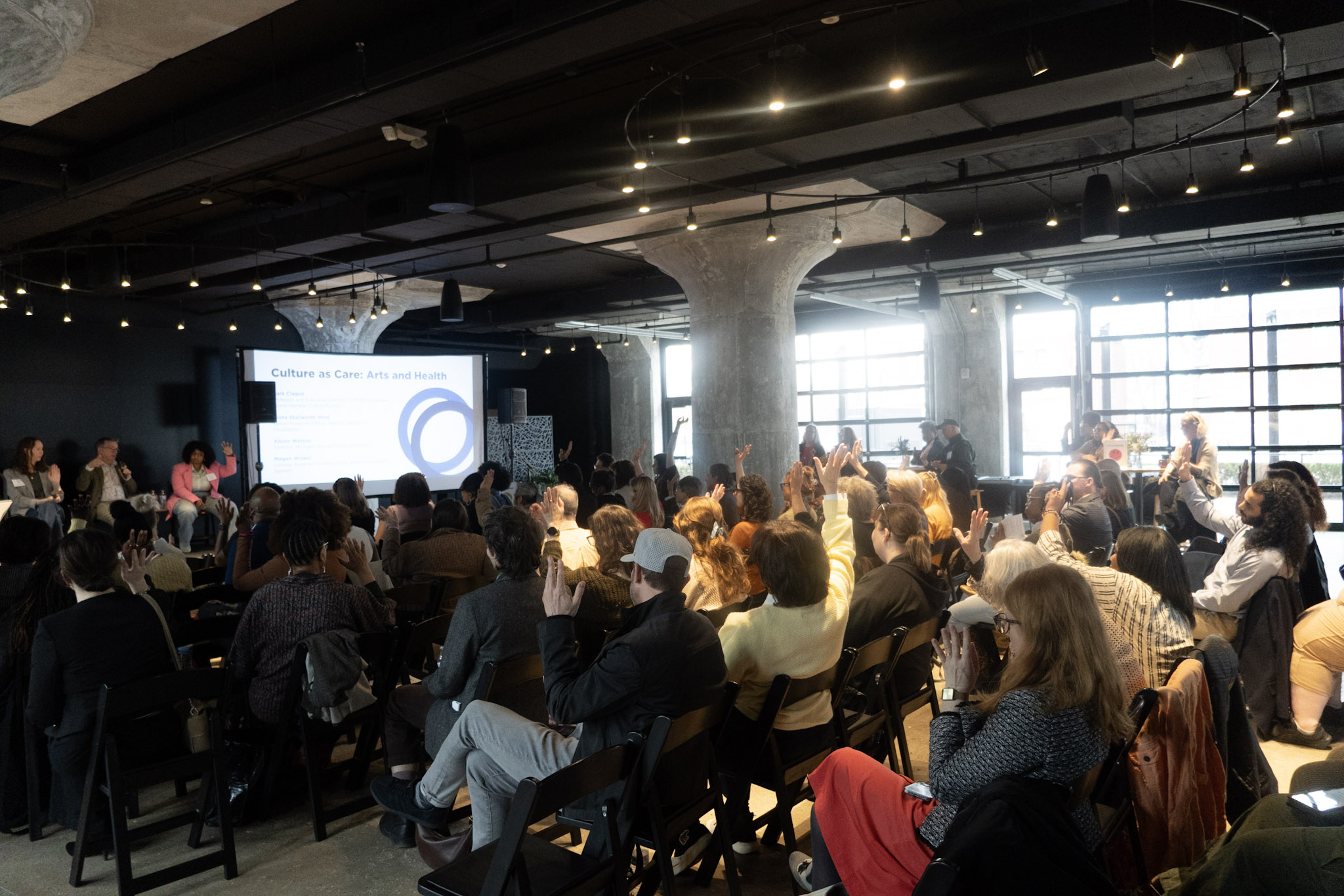 hands raised with panel discussion on stage